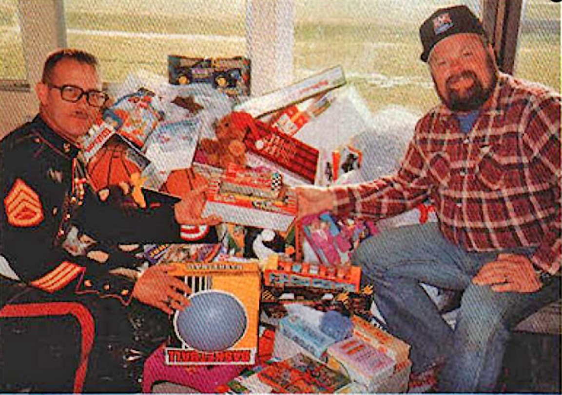 Marine Staff Sergeant Robert Siebenek and Flying Circuits (Ft. Wayne, IN) member Tim Fox with some of the stock of toys collected at the Circuits’ 1990 Toys for Tots fun fly. The club has collected and donated over 600 toys in the 3 years they have held t